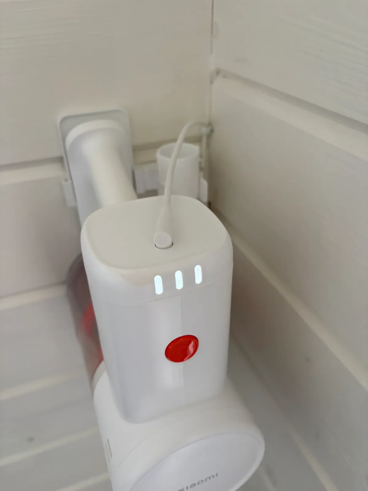 Cordless vacuum stored on its charger in the cleaning cupboard.
