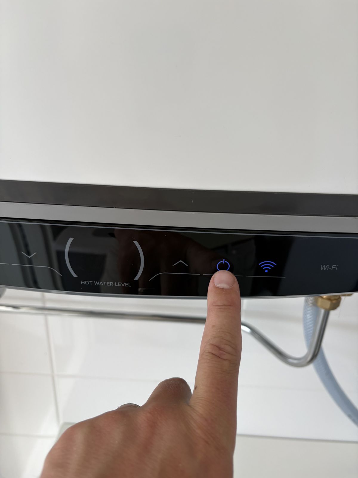 Ett finger trycker på varmvattenberedarens upplysta strömknapp.